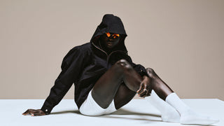 Person wearing a black hoodie with glowing eyes sitting on a white surface against a beige background